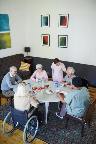 residents eating dinner at a care home with a carer checking on them