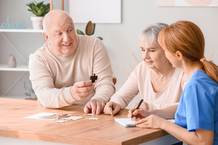 older person doing a puzzle in care home with staff